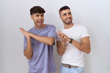 Sticker - Homosexual gay couple standing over white background clapping and applauding happy and joyful, smiling proud hands together