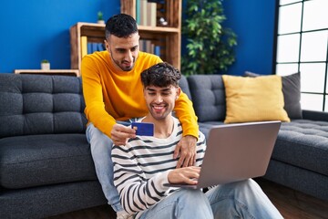 Wall Mural - Two man couple using laptop and credit cardsitting on sofa at home