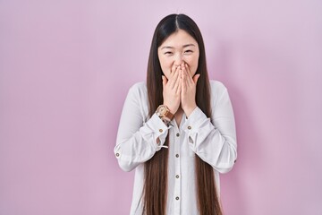 Poster - Chinese young woman standing over pink background laughing and embarrassed giggle covering mouth with hands, gossip and scandal concept