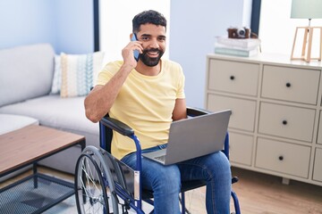 Wall Mural - Young arab man talking on smartphone sitting on wheelchair at home