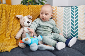 Adorable caucasian baby sitting on sofa with dolls at home