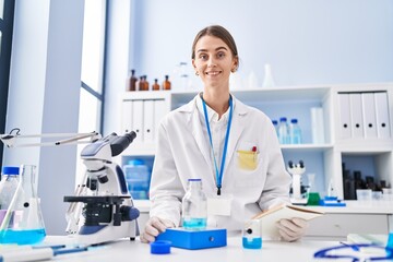 Poster - Young caucasian woman scientist weighing liquid reading notebook at laboratory