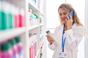 Wall Mural - Young beautiful hispanic woman pharmacist talking on smartphone holding shampoo bottle at pharmacy