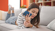 © Krakenimages.com - Young beautiful hispanic woman sending voice message by smartphone lying on sofa at home