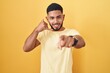© Krakenimages.com - Young hispanic man standing over yellow background smiling doing talking on the telephone gesture and pointing to you. call me.