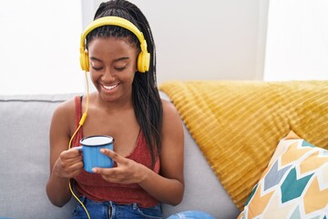 Wall Mural - African american woman listening to music drinking coffee at home