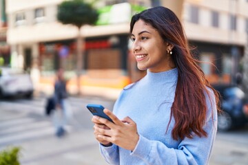 Poster - Young hispanic woman smiling confident using smartphone at street