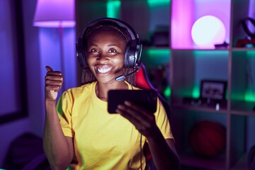 Wall Mural - African american woman playing video games with smartphone smiling happy and positive, thumb up doing excellent and approval sign