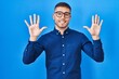 © Krakenimages.com - Young hispanic man wearing glasses over blue background showing and pointing up with fingers number ten while smiling confident and happy.
