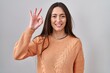 © Krakenimages.com - Young brunette woman standing over white background smiling positive doing ok sign with hand and fingers. successful expression.