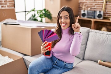 Poster - Young brunette woman moving to a new home choosing wall painting surprised with an idea or question pointing finger with happy face, number one