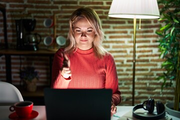 Canvas Print - Blonde woman using laptop at night at home smiling friendly offering handshake as greeting and welcoming. successful business.