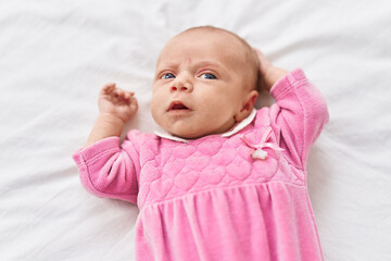 Adorable hispanic baby lying on bed with relaxed expression at bedroom