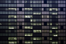 Seamless Skyscraper Facade With Blue Tinted Windows And Blinds At Night. Modern Abstract Office Building Background Texture With Glowing Lights Against Dark Black Exterior Walls. Created With AI.