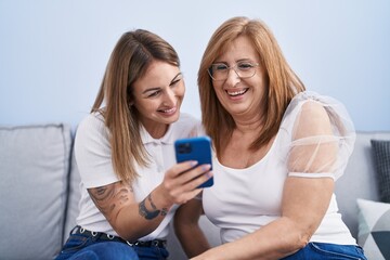 Sticker - Mother and daughter using smartphone sitting on sofa at home