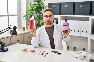 Sticker - Middle age caucasian dentist man holding mouthwash for fresh breath making fish face with mouth and squinting eyes, crazy and comical.