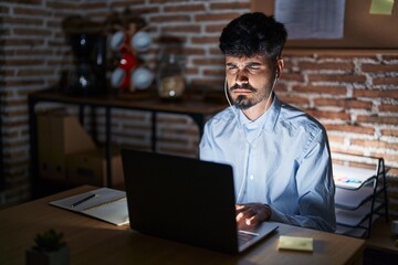 Wall Mural - Young hispanic man with beard working at the office at night skeptic and nervous, frowning upset because of problem. negative person.