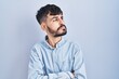 © Krakenimages.com - Young hispanic man with beard standing over blue background looking to the side with arms crossed convinced and confident