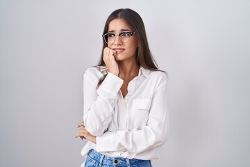 Poster - Young brunette woman wearing glasses looking stressed and nervous with hands on mouth biting nails. anxiety problem.