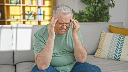 Canvas Print - Middle age grey-haired man suffering for headache sitting on sofa at home