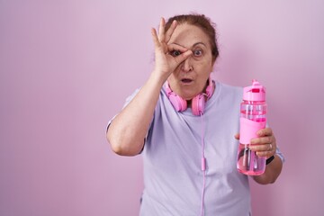 Sticker - Senior woman wearing sportswear and headphones doing ok gesture shocked with surprised face, eye looking through fingers. unbelieving expression.