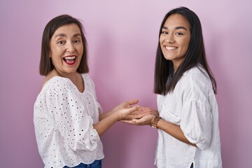 Wall Mural - Hispanic mother and daughter together pointing aside with hands open palms showing copy space, presenting advertisement smiling excited happy
