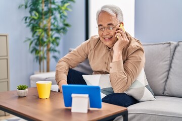 Canvas Print - Senior man talking on the smartphone watching touchpad at home