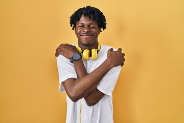 Sticker - Young african man with dreadlocks standing over yellow background hugging oneself happy and positive, smiling confident. self love and self care