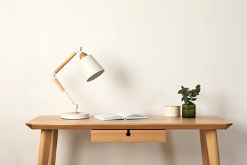 Wall Mural - Stylish modern desk lamp, open book and plant on wooden table near white wall