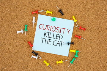 Curiosity killed the cat text on light blue post-it paper pinned on bulletin cork board surrounding by multi color pins. This message can be used in business concept about curiosity.