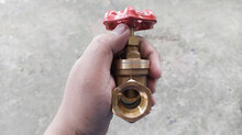 The Hand Hold A Brass Stop Valve By Front View ,valve Turning To Open Or Close The Water Flow.
