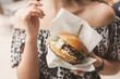 young woman holds a fast food burger in craft packaging in her hands. Street food. Woman has quick snack outside.
American unhealthy high-calorie food close-up