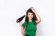 © Budjak Studio - A cute young girl dressed in a green top dries her beautiful long silky hair with a hair dryer against a white background.