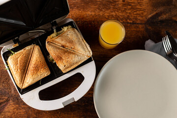 Toasted sandwiches on a toast sandwich, an empty plate and a glass of orange juice on a wooden background. Light morning breakfast, snack.