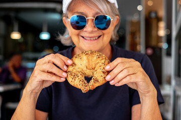 Sticker - Close up portrait of blurred smiling senior woman with blue sunglasses sitting at cafe table ready to eat a cereal croissant