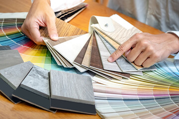 Wall Mural - Designer hand choosing and pointing at wood laminate material samples with color swatch and wooden tile texture collection nearby. Catalog guide for interior architecture and furniture design work