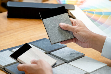 architect hand choosing sample of stone material or tile texture collection on the table in studio. 