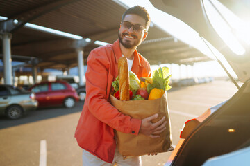 Wall Mural - Healthy food. Happy young man carrying grocery paper bag full of healthy vegetables and other food and drinks. Consumerism, sale, purchases, shopping, lifestyle concept.