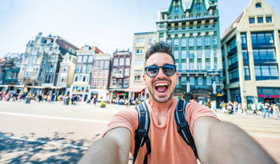 Wall Mural - Happy tourist taking selfie picture in Amsterdam, Netherlands - Cheerful man using smart mobile phone device outside - Student traveler enjoying summer european vacation - Life style tourism concept