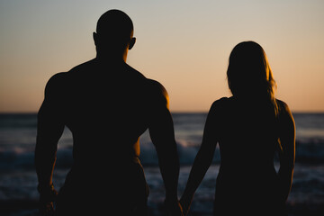 A couple stands on the beach and sees off the sunset. Dramatic view of the calm sky. Man and woman are holding hands.