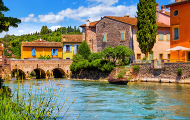 Borghetto Valeggio sul Mincio, Verona, Italy. Italian traditional village with vintage colorful houses above river. Stone bridge among ancient architecture. Among flowers and greens. Summer sunny day