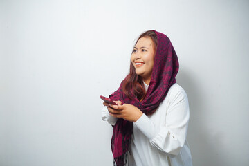 A portrait of a happy Asian Muslim woman wearing a hijab, holding her phone, isolated by white background