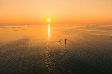 Poster - Aerial view of two people on stand up paddle boards on quiet sea at sunset. Warm summer beach vacation holiday.
