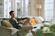 © imtmphoto - young asian man sitting in family couch in living room at home looking at mobile phone