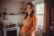 © igolaizola - Portrait of a beautiful pregnant woman in orange dress at home.