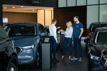 The seller hands over the car keys to the buyers. The couple bought a new car.