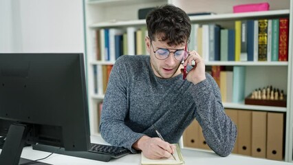 Canvas Print - Young hispanic man student talking on smartphone writing on notebook at library university