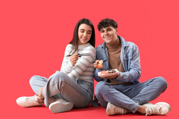 Wall Mural - Young couple eating sushi on red background