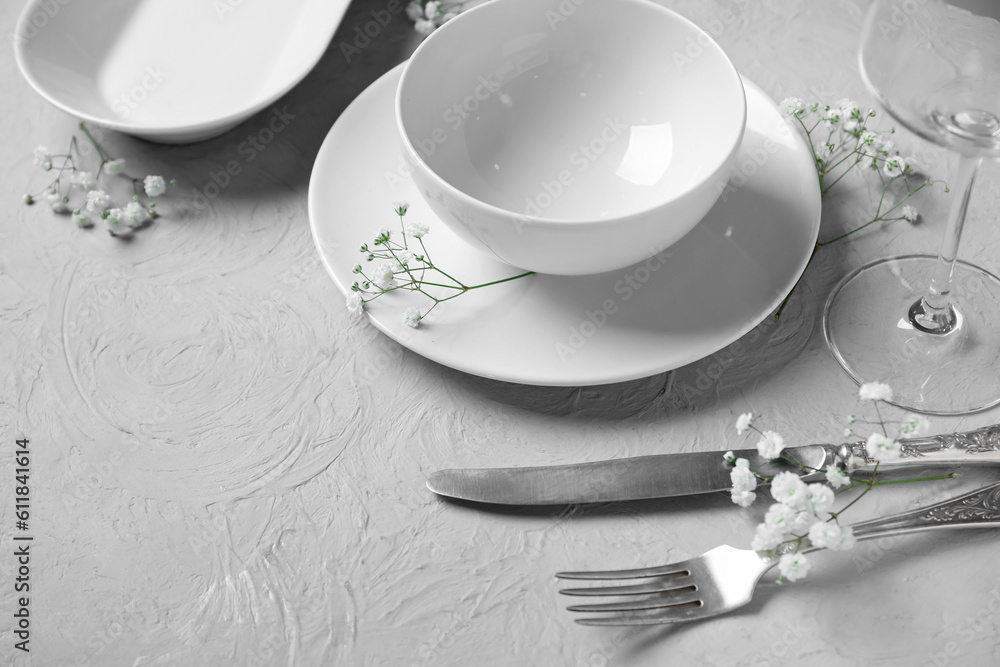 Plates with silver cutlery, flowers and glass on grunge grey background