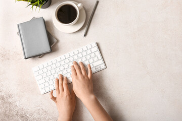 Female programmer using computer keyboard with cup of coffee and notebooks on light background